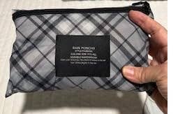 Person holding a compact, plaid-patterned rain poncho pouch with a brand label