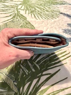 Hand holding a full wallet with cards and cash, on a patterned surface
