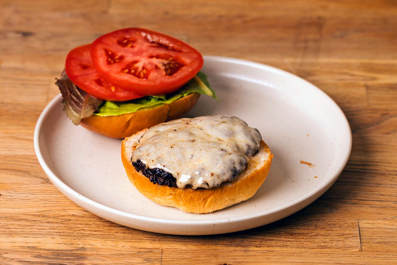 Provolone burger with melted cheese on a bun served openfaced with lettuce and tomato slices on the top bun on a plate
