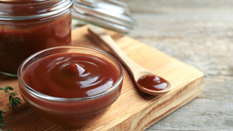Barbecue sauce in a small glass bowl next to a small wooden spoon with barbecue sauce.