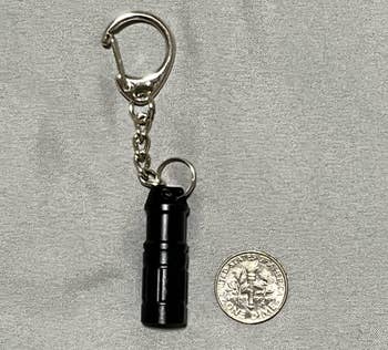 Compact black keychain flashlight next to a quarter for size comparison
