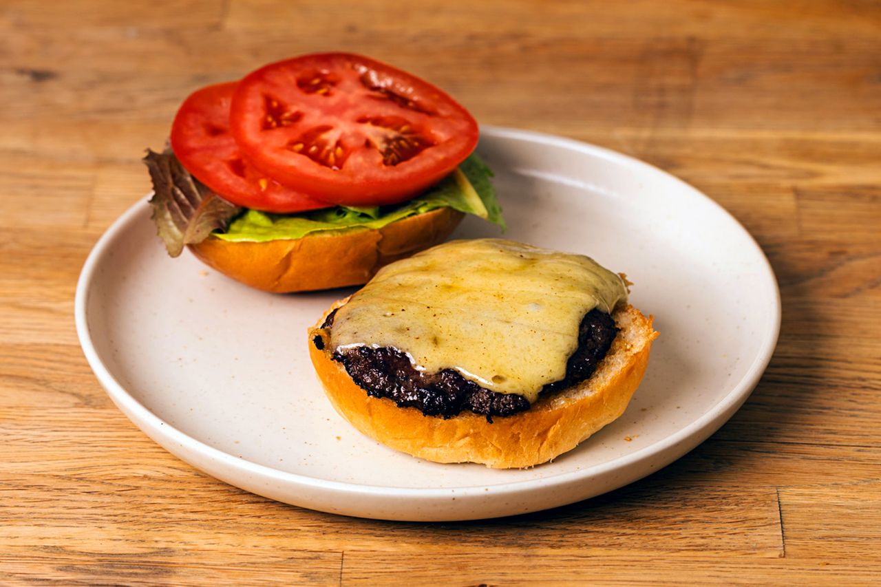Gruyère cheeseburger on a plate with the top bun open showing melted cheese tomatoes and lettuce