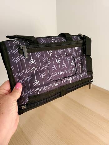 Hand holding a black travel organizer with arrow patterns, featuring zipper compartments