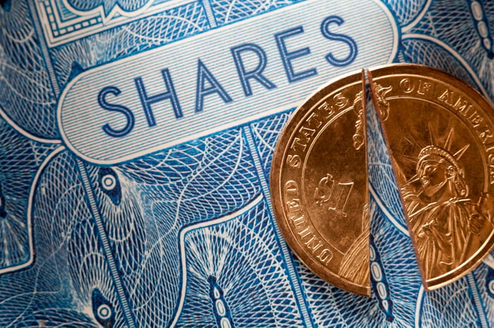 A U.S. dollar coin split in half and placed atop a paper stock certificate for shares of a company.