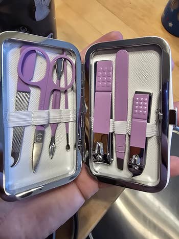 hand holding Manicure kit with scissors, nail clippers, tweezers, and a file in a compact case