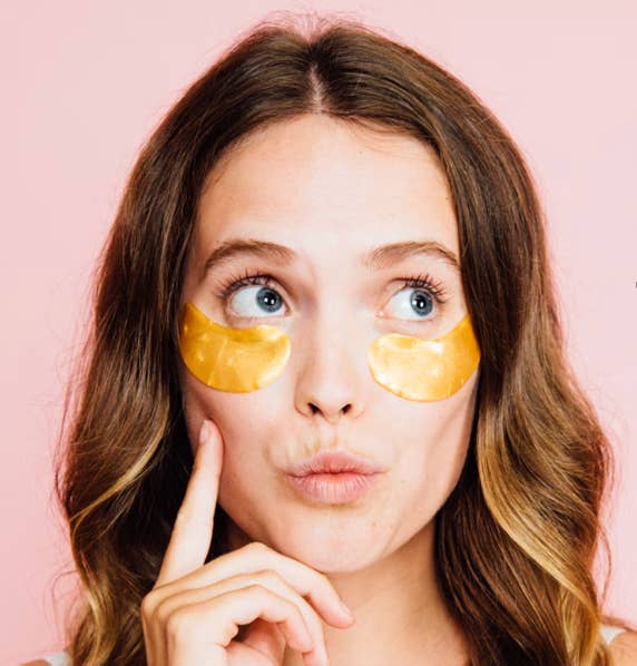 Person with gold under-eye patches looking thoughtful against a plain background