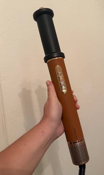 Person holding a handheld hair styling tool with a cylindrical design and buttons on the handle
