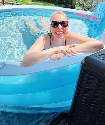 Person in a pool, smiling and relaxing, wearing sunglasses and a swimsuit. The setting appears casual and summery