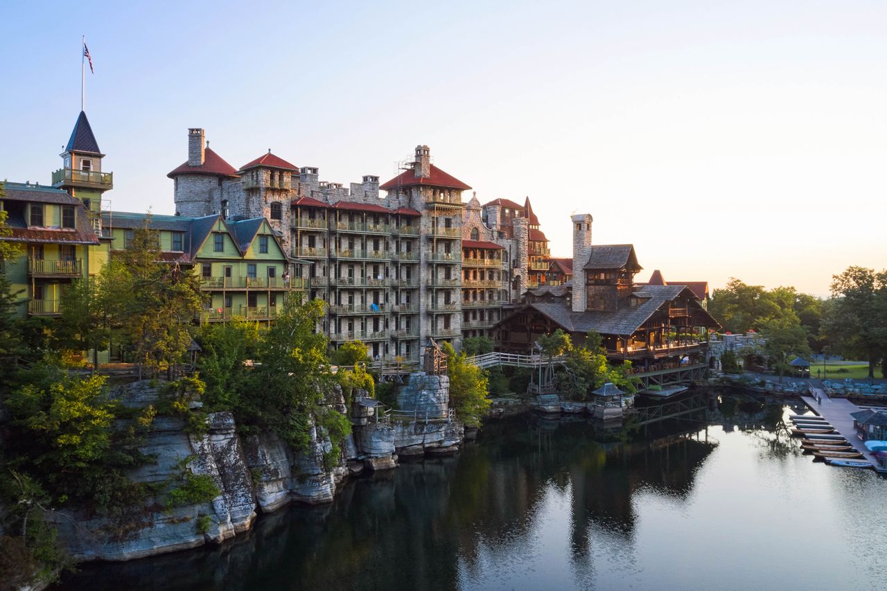 An expansive resort building near a tranquil lake surrounded by natural scenery showcasing an architectural design with multiple levels and towers