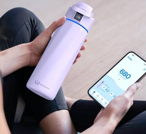 Person holding a smart water bottle and a smartphone displaying hydration stats