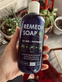 Hand holding a 12 oz bottle of Remedy Soap with tea tree, mint, and aloe for foot and body, described as soothing and deodorizing