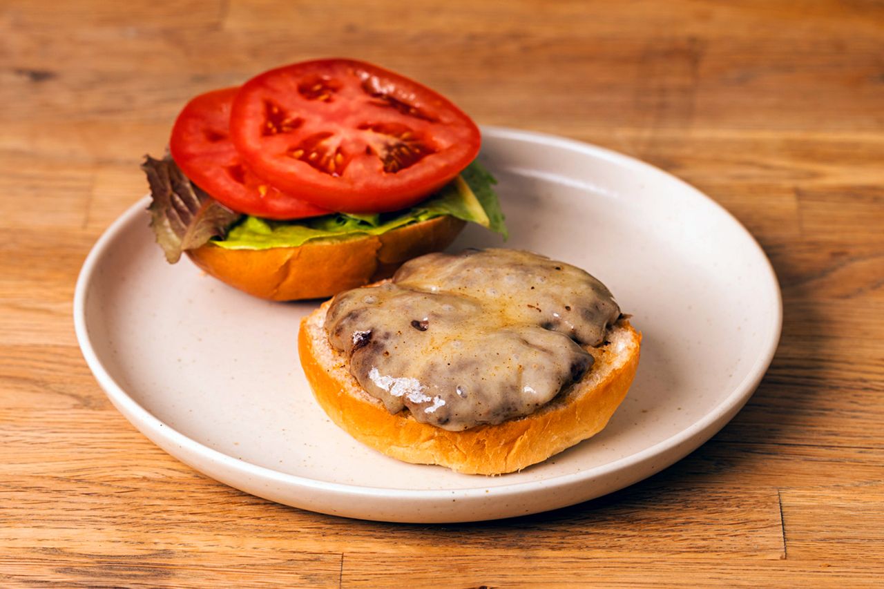 A burger with melted Swiss cheese and a top bun with lettuce and tomato on a plate
