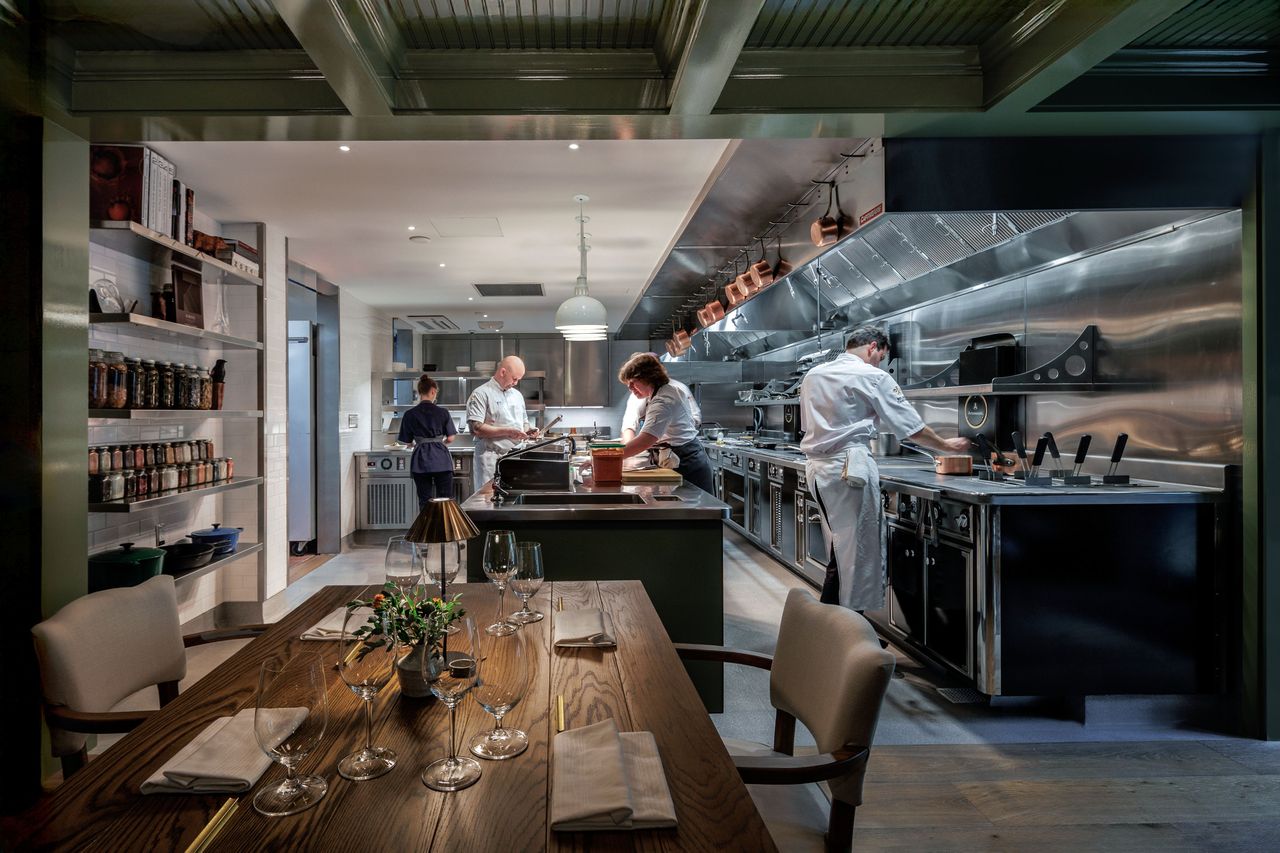 Chefs working in a professional kitchen viewed from a dining area with a set table