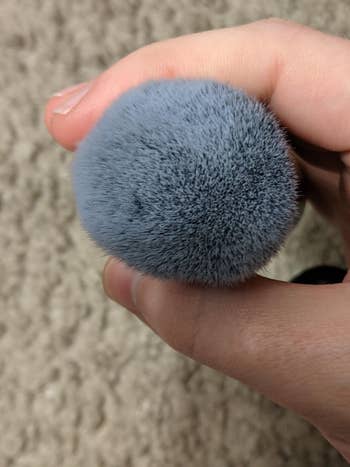 Close-up of a fluffy makeup brush held between fingers, showcasing soft bristles