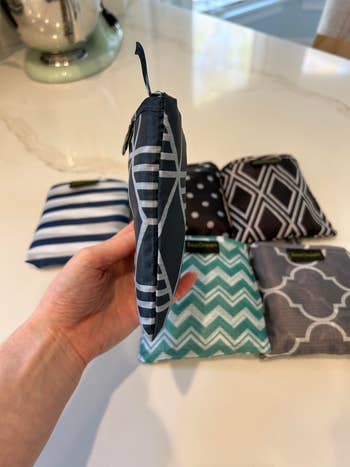 a hand holding the collapsible shopping bag with other folded bags in the background