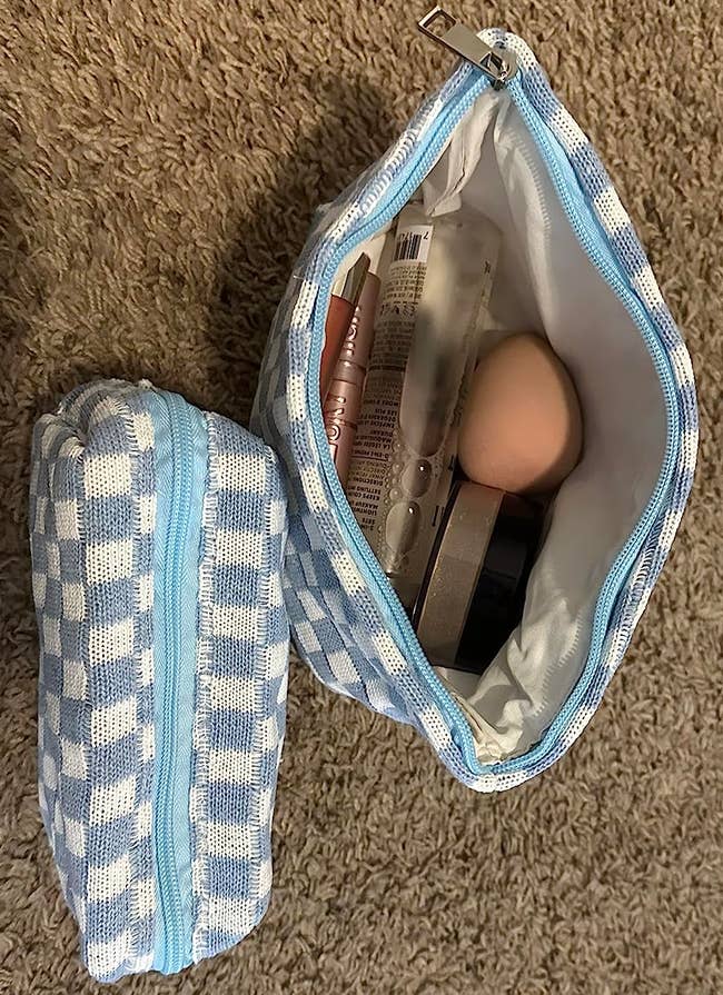 Open and closed checkered makeup bags on the floor, showing cosmetics inside, including a beauty sponge and makeup palette