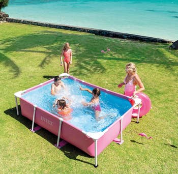 Family enjoys a rectangular above-ground pool set on grass near a beach. An adult holds a float next to the pool