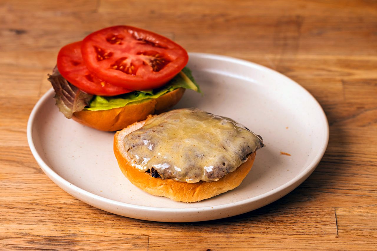 Cheddar cheeseburger on a plate with melted cheddar cheese sliced tomatoes and lettuce