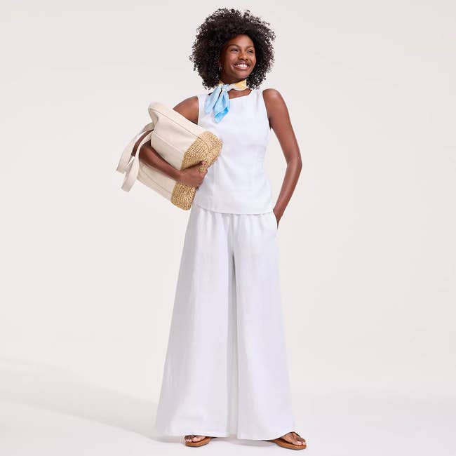 Woman smiling, wearing a sleeveless top and wide-leg pants, holding a large tote bag, suitable for a casual summer look