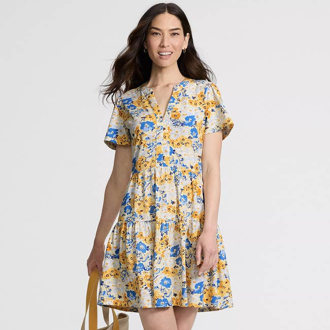 Woman in a floral print dress holding a tote bag, smiling and looking forward