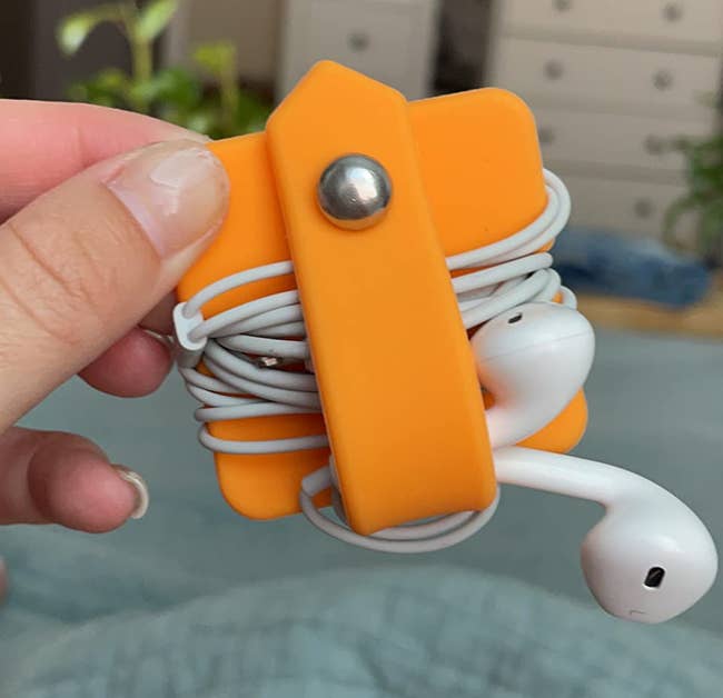 Hand holding white earphones neatly wrapped in an orange cord organizer