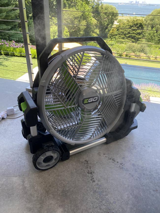 Portable outdoor fan on a patio with misting feature, overlooking a garden and pool
