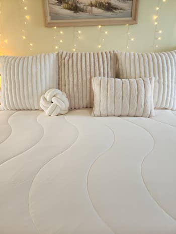 Luxurious bedroom setup featuring plush pillows and a decorative knot cushion on a neatly made bed with a wavy pattern comforter