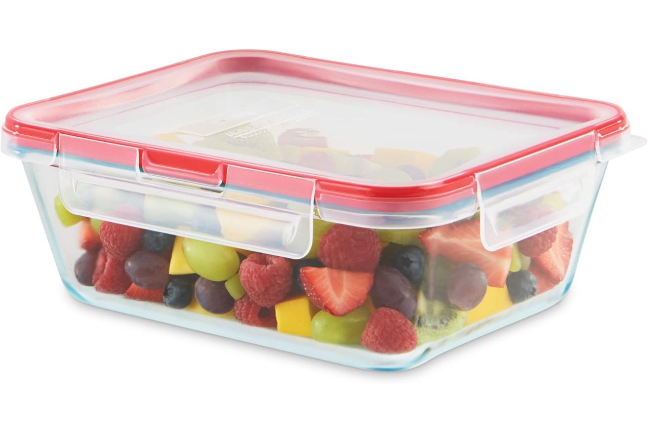 A food storage container with a transparent lid filled with an assortment of fruits such as strawberries grapes and mango pieces