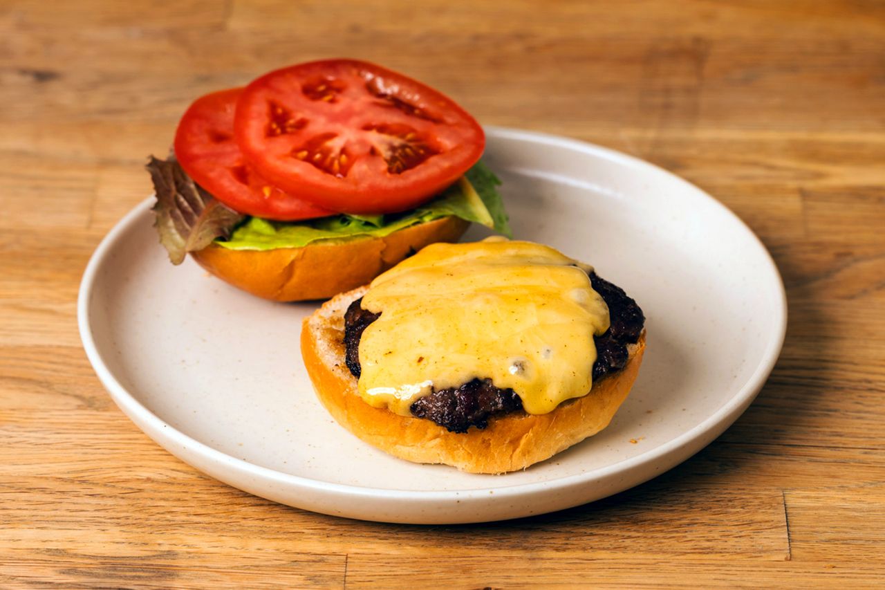 Gouda cheeseburger on a plate with the top bun aside showing lettuce and tomato slices