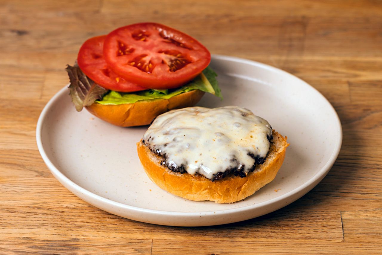 An open hamburger with melted cheese on the patty served on a white plate with lettuce and tomato slices on the top bun
