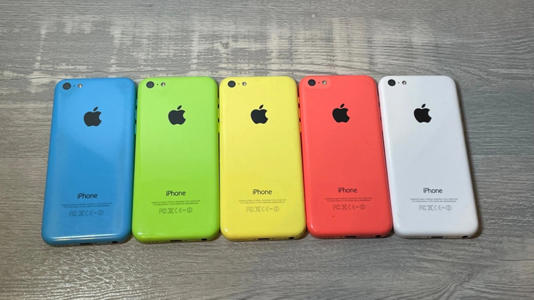 Five iPhone 5c phones lying side by side. From the left, they're colored blue, green, yellow, a coral pink, and white