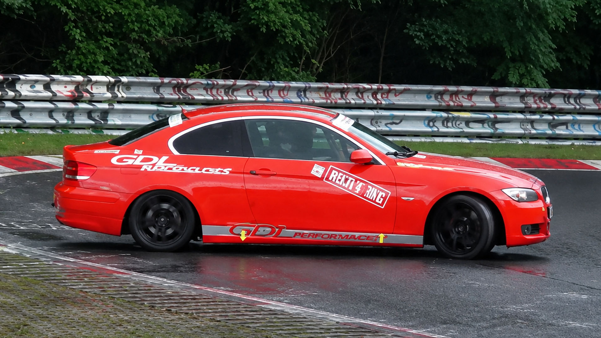 Red coupe balances traction through slippery Nürburgring corner under rain