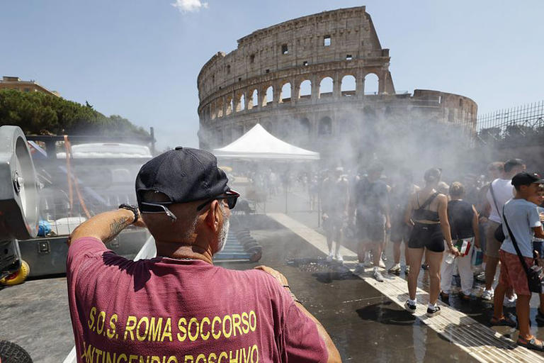 A volunteer cools off tourists under mist cannons set by the Civil Protection in front of the Colosseum in Rome