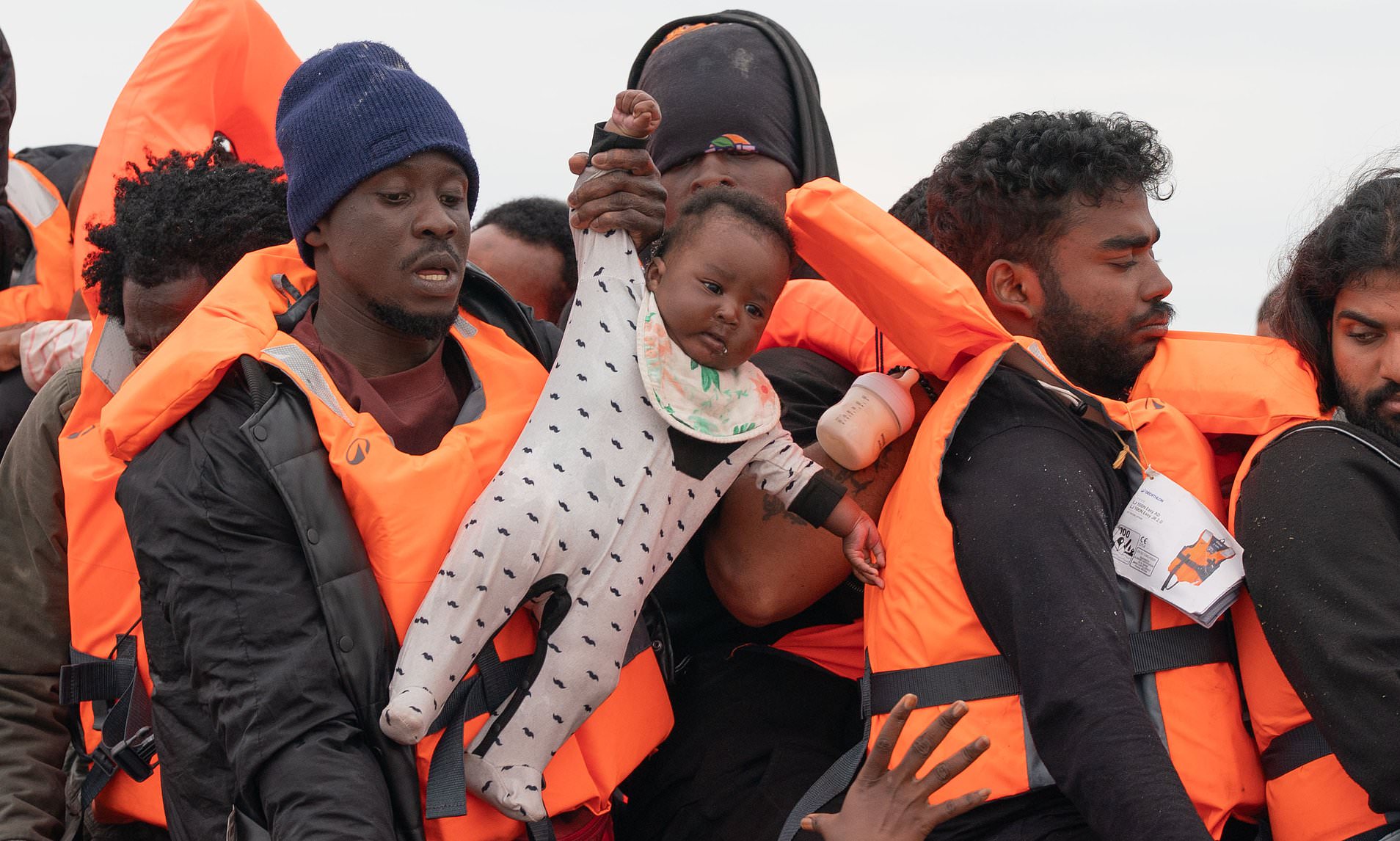 French police stand and watch as months-old baby is carried aboard packed dinghy headed for Britain