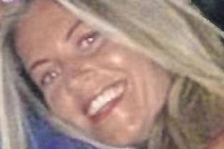 A close-up portrait of a woman with blonde hair, smiling brightly and looking directly at the camera. The background is blurred, focusing attention on her face and expression.