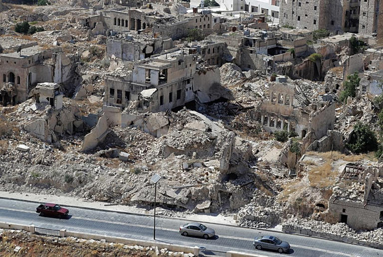 FILE: People drive their cars past destroyed buildings in the city of Aleppo, 16 August 2018 AP Photo