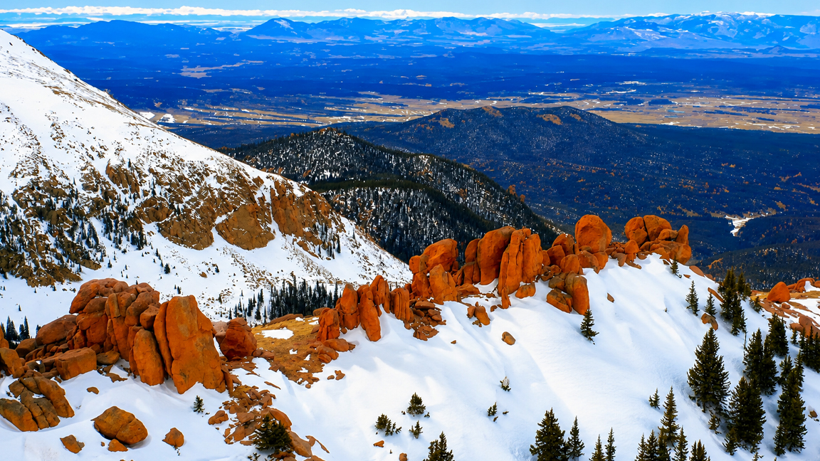 Orange rock formations rising through a snowy mountain landscape