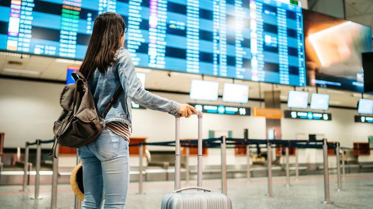 Young Asian female tourist checking the arrival departure board at airport in Budapest.