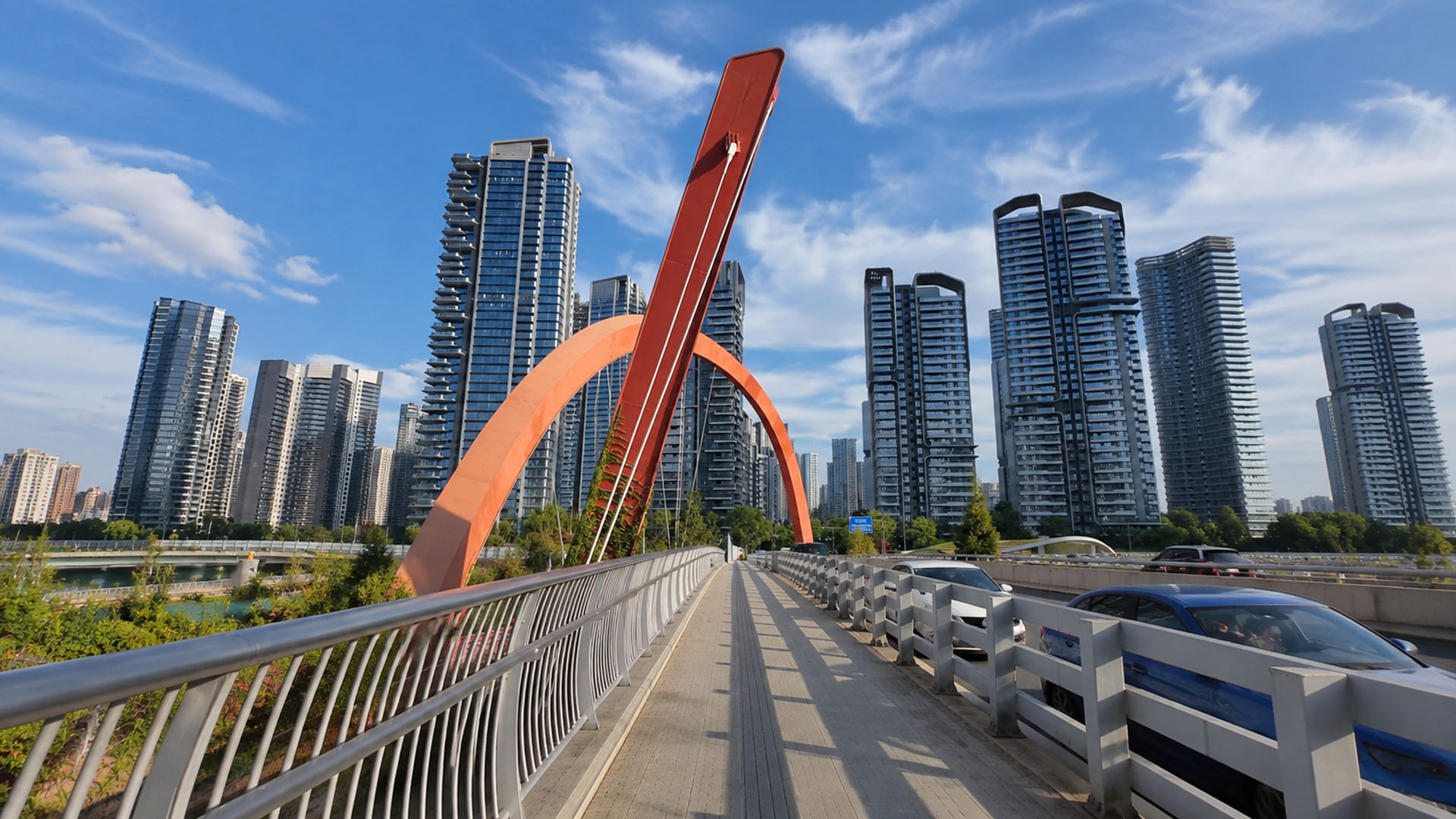 Wide pedestrian walkway runs along striking orange bridge above modern ...