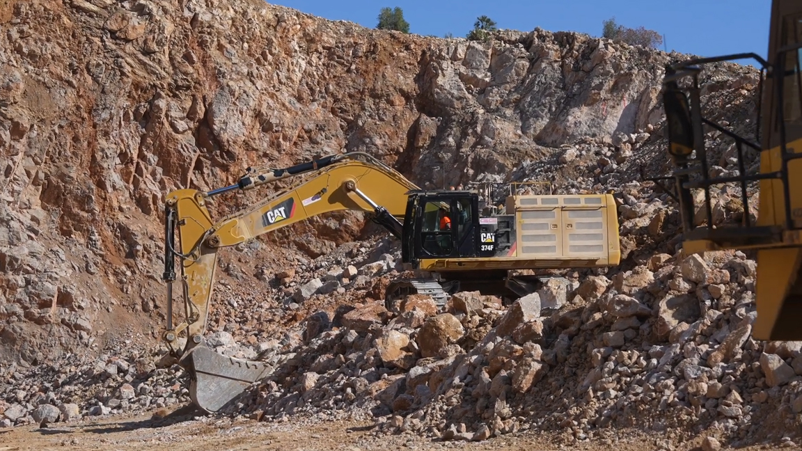 Heavy excavator breaking and loading rock in a large quarry