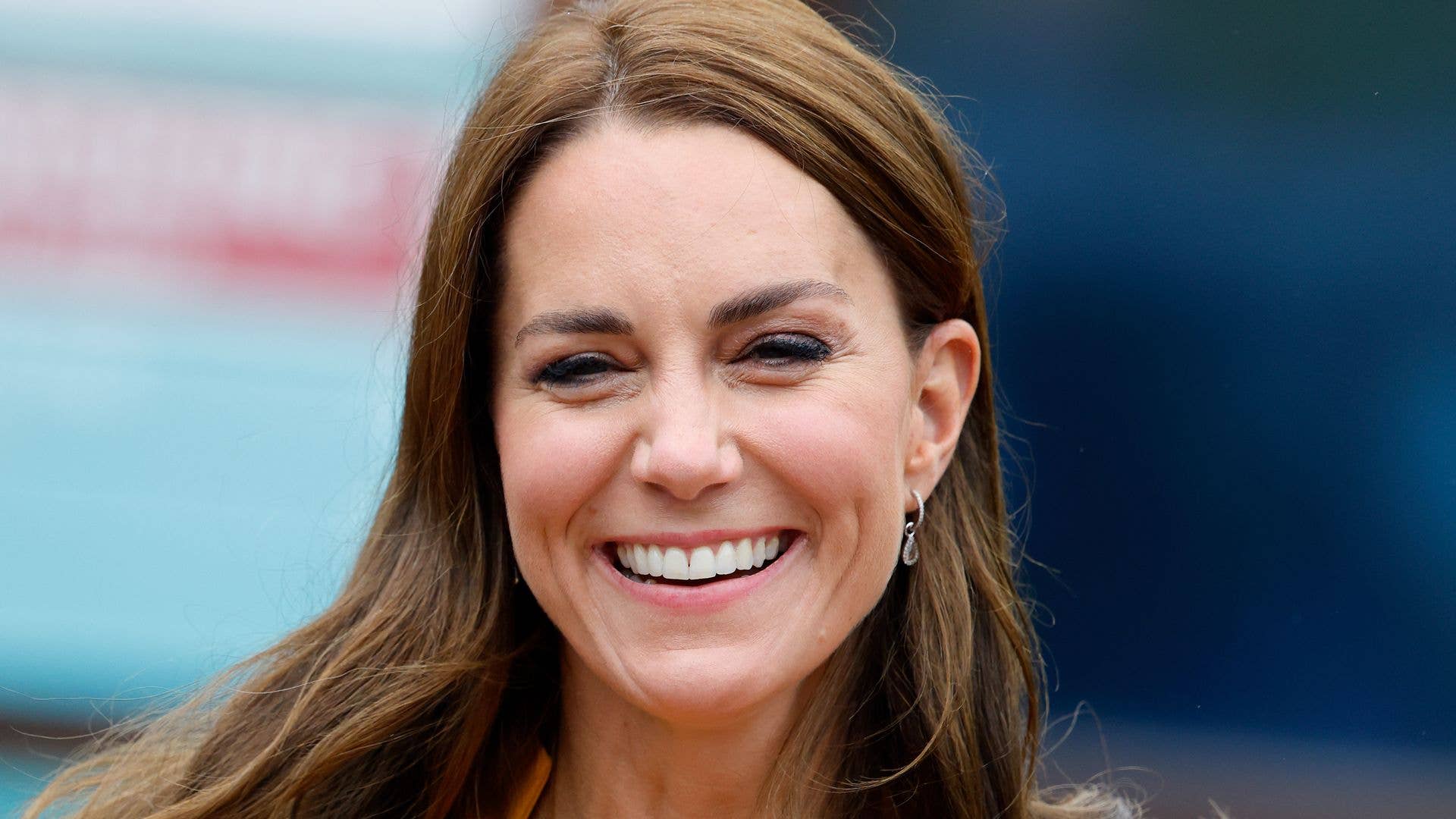 Kate Middleton, wearing a yellow blazer, smiles brightly while holding a bouquet of flowers.
