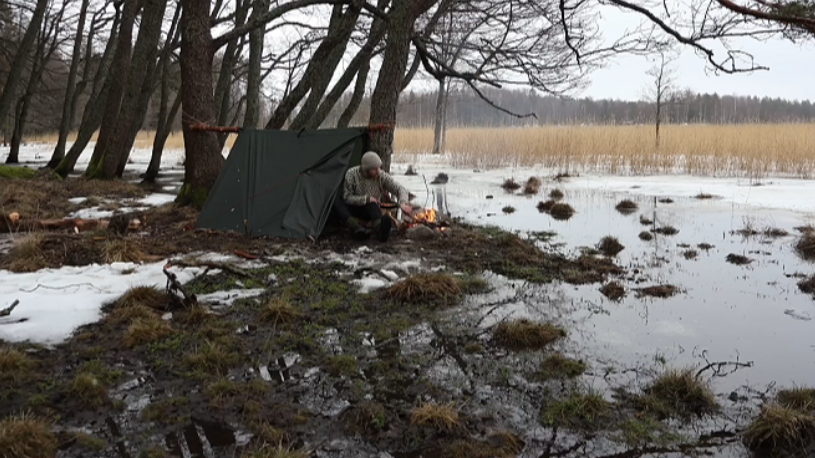 Snow camping adventure in frozen wetlands with tarp tent setup