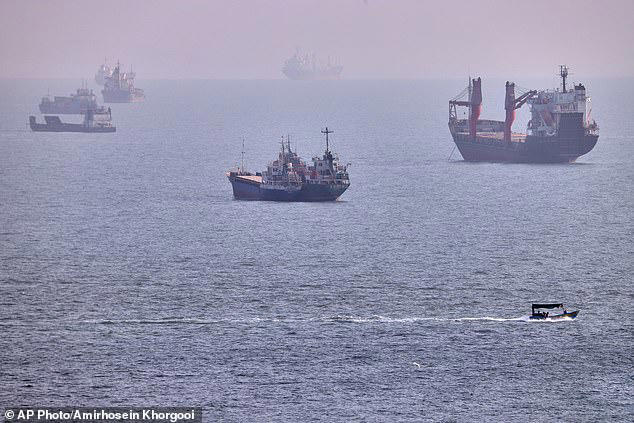 A small boat sails past cargo ships and other commercial vessels anchored in the Strait of Hormuz off Bandar Abbas, Iran, Wednesday, August 5