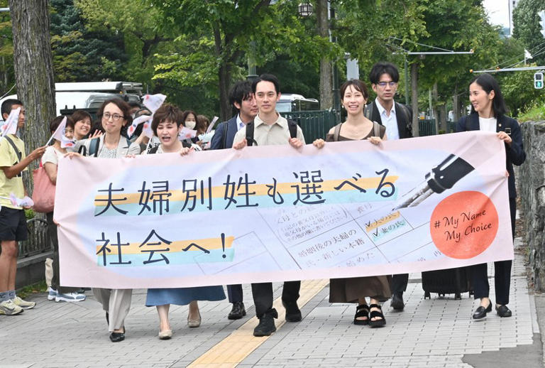 Plaintiffs Kiyotaka Nishi, center, and Mana Sato, third from right, arrive at the Sapporo District Court in Sapporo's Chuo Ward, July 29, 2026. The banner reads, "Toward a society where married couples can also choose to have separate surnames." (Mainichi/Yukika Wada)