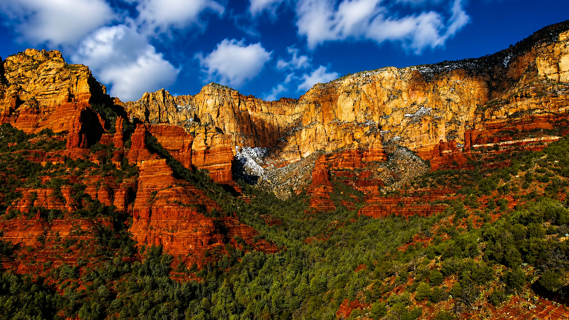 Sunlight reveals the fiery layers of towering red cliffs