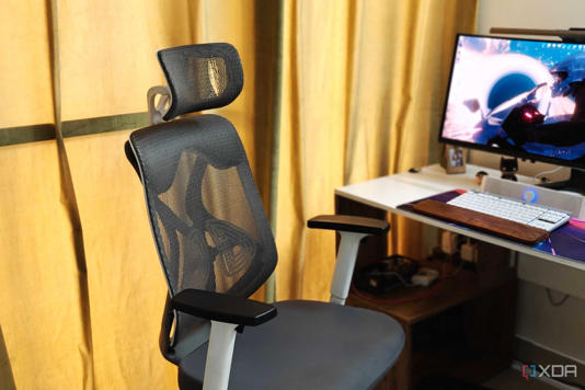 A grey ergonomic chair against a yellow background next to a PC desk