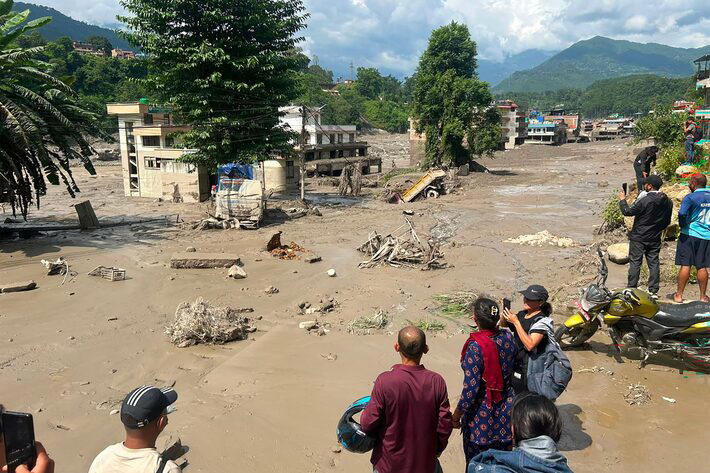 Moradores observam casas parcialmente submersas em águas barrentas após enchentes repentinas em Trishuli Bazar, no distrito de Nuwakot, no Nepal. Foto: Prakash Mathema/AFP