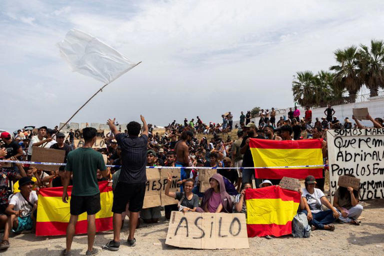 Migrants hold Spanish flags and signs calling for asylum as they gather in Ceuta, Spain, August 16, 2026. REUTERS/Maria Alejandra Cardona   TPX IMAGES OF THE DAY