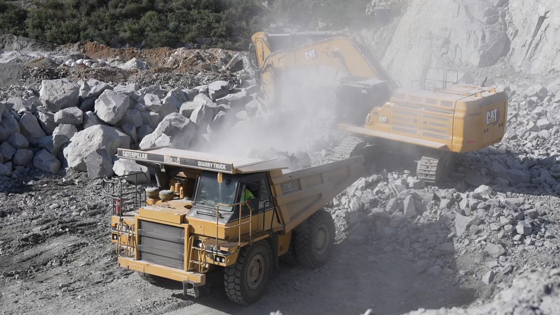 Massive CAT excavator loading a quarry truck with giant rocks