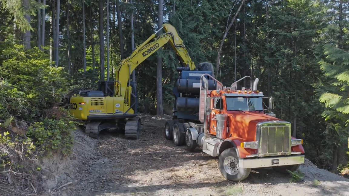 Kobelco excavator loads massive tires onto a logging truck